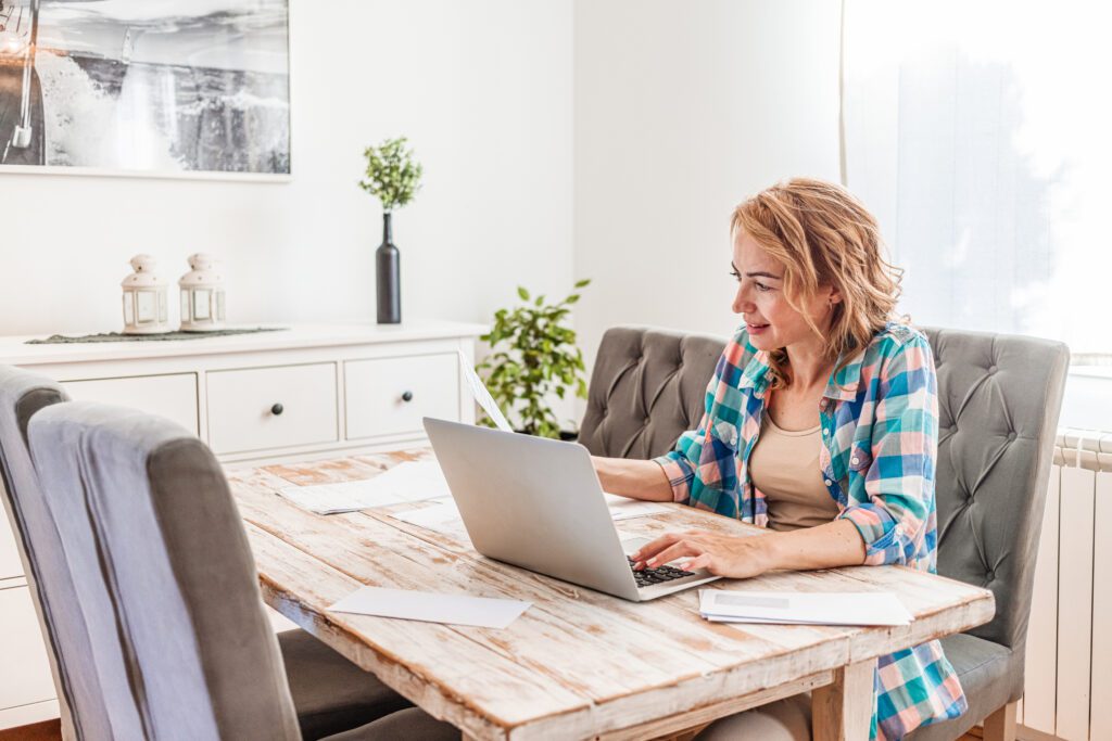Woman doing paperwork and using laptop wearing casual clothes