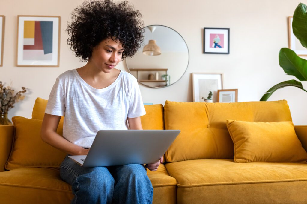 Young woman sitting on the couch using laptop working at home.