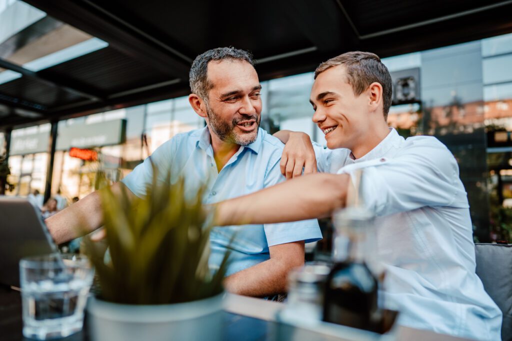 Handsome and happy father and his teenager son sitting in a restaurant and talking.