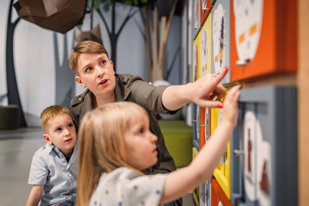 Mother playing discovery games with two little children in an interactive natural history museum exhibition. Learning through play concept.