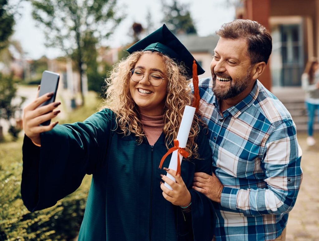 Happy university graduate and her father having fun while taking selfie with smart phone.